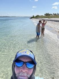 A group enjoys a sunny day at the beach, with one person taking a selfie while others play in the shallow water — a perfect sandbar stop for fun and relaxation.
