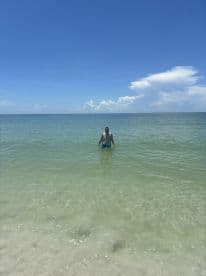 A man wades in the clear waters of a beautiful beach, enjoying a sunny day by the sea — perfect for relaxation and aquatic adventures.