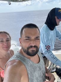 A fun selfie of a couple enjoying their time on the boat with a captain at the helm, capturing the excitement of their on-water adventure.