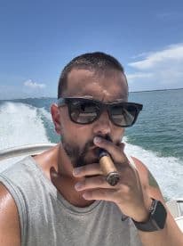 A man enjoys a cigar while cruising on a boat under a clear blue sky, capturing the essence of relaxation on the water.