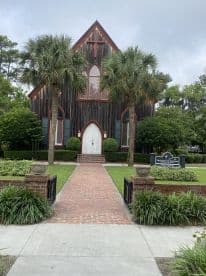 A charming church building surrounded by lush greenery and palm trees, showcasing unique architectural features.