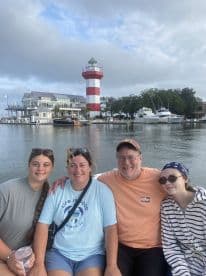 A cheerful family poses on a boat with a striking lighthouse in the background, capturing a memorable moment on the water.