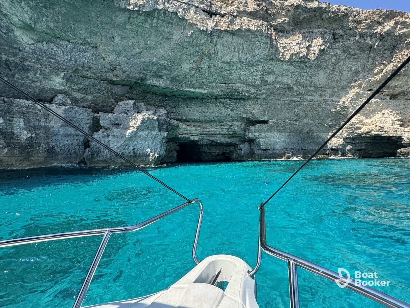 A stunning view of a boat approaching a rocky coastline with a cave entrance, surrounded by crystal-clear turquoise waters — perfect for exploring hidden gems on a boating adventure.