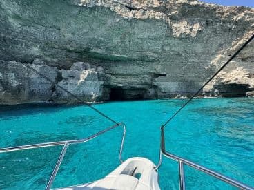 A stunning view of a boat approaching a rocky coastline with a cave entrance, surrounded by crystal-clear turquoise waters — perfect for exploring hidden gems on a boating adventure.