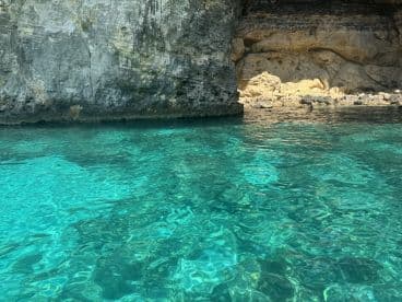 A stunning view of crystal-clear waters near a rocky coastline, with people enjoying the serene environment — perfect for exploring hidden gems and natural beauty.