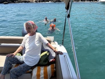 A serene moment on a boat with a woman relaxing while others enjoy swimming nearby — a perfect snapshot of a fun day on the water.