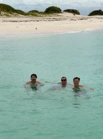 A group of friends enjoys a refreshing swim in crystal-clear waters, surrounded by a beautiful beach — perfect for a fun day out on the water.