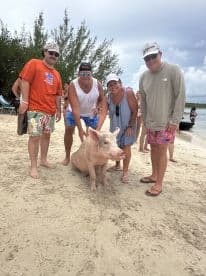A group of friends interacts with a friendly pig on the beach, capturing a unique wildlife experience in the Bahamas.