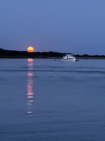 A serene sunset view featuring a boat gently cruising on calm waters, with the sun setting on the horizon, creating a picturesque scene perfect for evening boat outings.