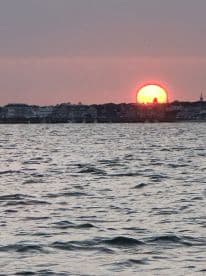 A stunning sunset over the coastline, reflecting on the water's surface, creating a picturesque scene perfect for evening boat cruises.