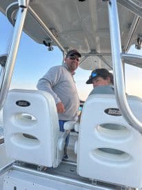 Two individuals are seated at the helm of a boat, showcasing the comfortable interior and seating arrangement — perfect for a day on the water.