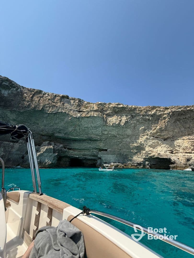 A stunning view of a boat near a rocky coastline with crystal-clear waters, showcasing the beauty of a perfect day on the water.