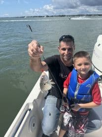 A father and son share a joyful moment while fishing, showcasing their catch on a sunny day — a perfect family adventure on the water.