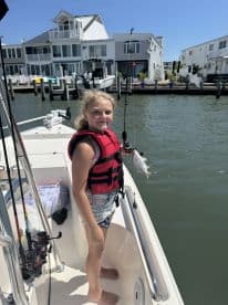 A young girl proudly holds her catch while fishing from a boat, showcasing the joy of a family fishing trip on the water.