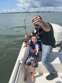 A joyful father and son celebrate their fishing catch aboard a boat, showcasing a perfect family bonding experience on the water.