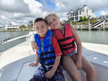 Two children wearing life jackets smile for the camera while enjoying a day on the boat, capturing the joy of family adventures on the water.