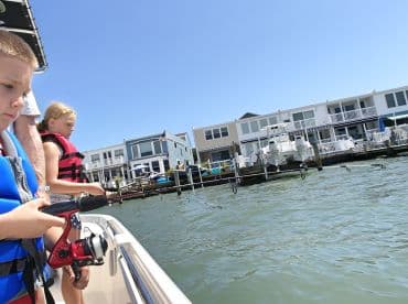Two children enjoy a fishing trip from a boat, showcasing a fun family experience on the water with a scenic waterfront backdrop.