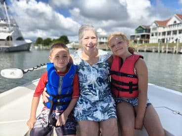 A joyful family moment aboard a boat, featuring a grandmother and her two grandchildren wearing life jackets, perfect for creating lasting memories on the water.
