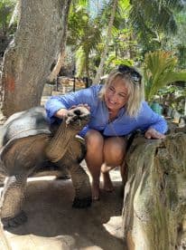 A woman interacts with a giant tortoise in a lush tropical setting, showcasing a unique human-animal connection in a wildlife experience.