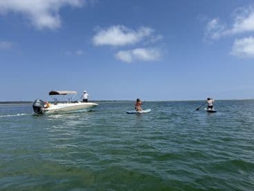 A group enjoys a sunny day on the water, with one person paddleboarding while another operates a boat nearby — perfect for summer adventures and water sports.