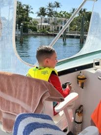 A young boy in a life jacket sits at the helm of a boat, ready for an adventure on the water. The interior cabin setting showcases the boat's features and safety gear.