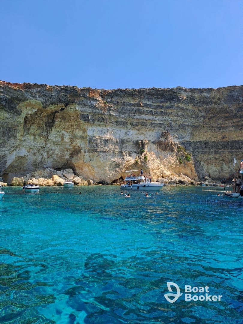 A vibrant scene of swimmers enjoying the crystal-clear waters near a stunning coastline, with boats anchored nearby — a perfect destination for a summer adventure.