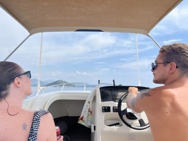 A couple enjoys a scenic boat ride, with one steering and the other taking in the views — perfect for adventure seekers on the water.