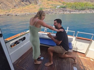 A romantic proposal takes place on a boat, capturing a joyful moment between a couple against a stunning backdrop — perfect for unforgettable love stories on the water.