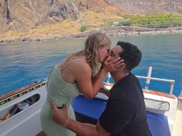 A couple shares a romantic kiss aboard a boat, surrounded by stunning coastal scenery — perfect for intimate moments on the water.