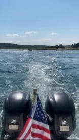 A scenic view from the back of a boat, showcasing the engines and an American flag as it cruises through sparkling waters, perfect for summer adventures.