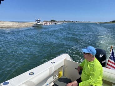 A man relaxes on a boat while cruising near a beach, enjoying the sunny day and scenic views — a perfect moment for boating enthusiasts.