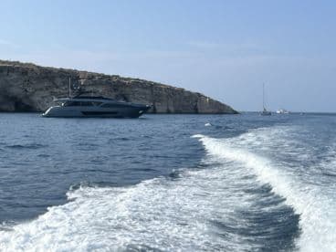 A sleek yacht navigates the waters near a rocky coastline, showcasing the beauty of boating adventures in serene surroundings.