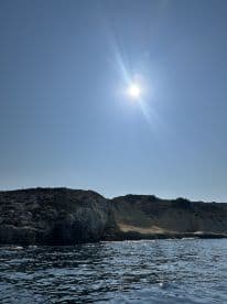 A scenic view of a rocky coastline under a bright sun, capturing the essence of a tranquil day on the water.