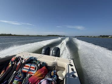 A scenic view from the back of a boat cruising through calm waters, showcasing the beautiful landscape and wake created by the vessel.