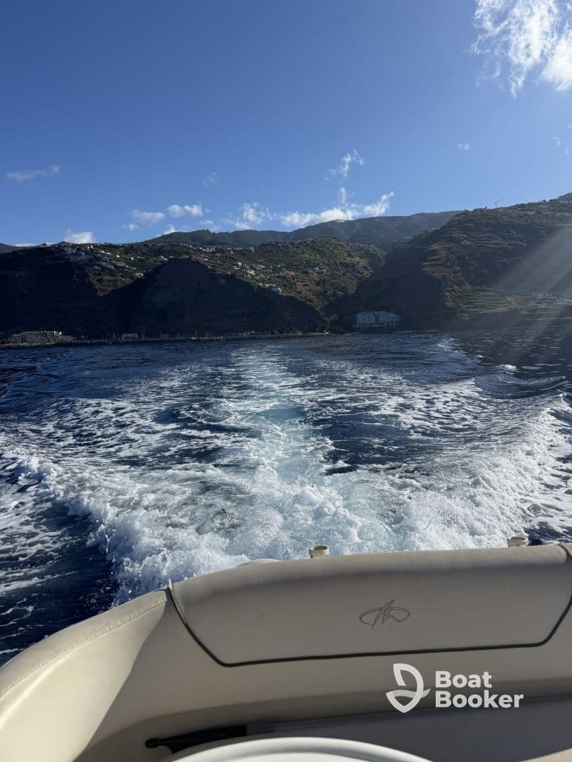 A scenic view from the bow of a boat cruising through clear waters, with lush hills and a coastal landscape in the background.