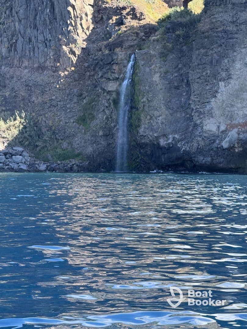 A stunning view of a waterfall cascading down rocky cliffs into turquoise waters, showcasing the natural beauty of the coastline.