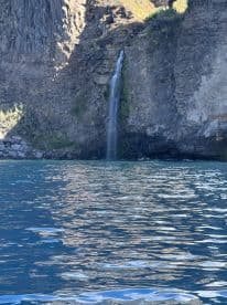 A stunning view of a waterfall cascading down rocky cliffs into turquoise waters, showcasing the natural beauty of the coastline.