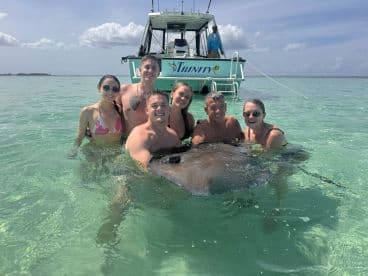 A group of six enjoys a memorable encounter with a stingray in shallow waters, showcasing the thrill of wildlife interactions during their boating adventure.