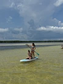 Two girls enjoy paddleboarding in shallow waters, showcasing a fun day of water activities under a bright sky.