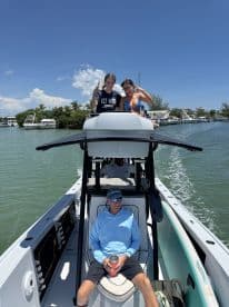 Two friends pose playfully on the bow of a boat while another relaxes in the seating area, capturing a fun day on the water.