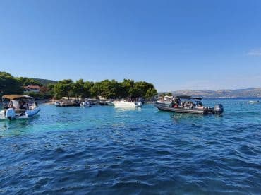 A lively scene of multiple boats filled with guests enjoying a sunny day on the water, surrounded by beautiful turquoise waters and lush greenery.