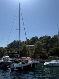 A picturesque view of a yacht docked in a serene harbor, surrounded by lush greenery and clear blue skies — perfect for showcasing boating adventures.