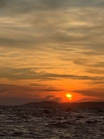 A stunning sunset over the ocean, with silhouetted islands in the background — a perfect moment for capturing the beauty of nature while on a boating adventure.