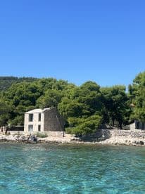 A picturesque view of a rocky coastline with a charming stone building surrounded by lush greenery, perfect for capturing the serene beauty of island life.