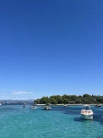 A picturesque view of several boats anchored in crystal-clear turquoise waters, surrounded by lush greenery and a clear blue sky, perfect for a day of relaxation and exploration.
