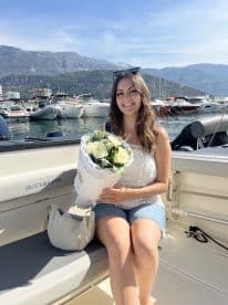 A joyful woman holds a bouquet of flowers while sitting on a boat, capturing a moment of celebration amidst a scenic marina backdrop.