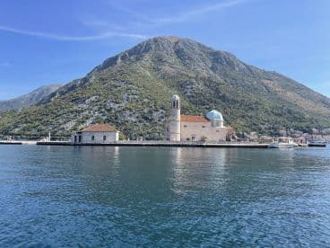 A picturesque view of a historic landmark on the waterfront, surrounded by lush mountains and clear waters — a perfect destination for sightseeing and exploration.