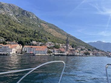 A picturesque view of a charming coastal town with historic architecture and lush mountains, perfect for exploring by boat.