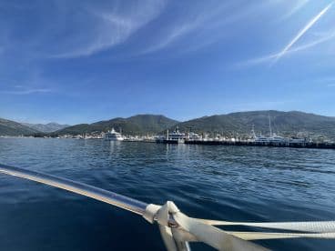 A serene view from a boat showcasing a marina filled with yachts against a backdrop of lush mountains and a clear blue sky, perfect for a day on the water.