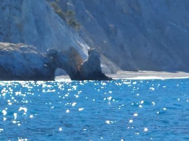 A stunning view of a natural rock arch along the coastline, surrounded by sparkling turquoise waters — a perfect destination for boat tours and scenic explorations.